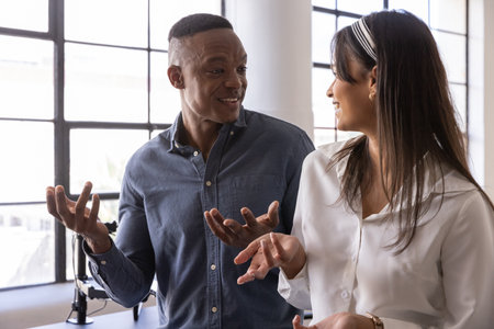 Diverse coworkers talking and gesturing at office desk with microphone arm and grid windows. Professional, collaboration, communication, modern, corporate, dialogue, technologyの写真素材
