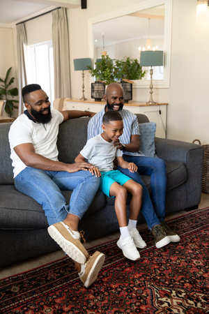 African American family laughing on dark grey sofa in living room with red and black rug. Family,...