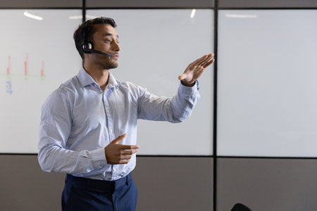 Asian male dress shirt wearing headset microphone pointing at whiteboard with line graphs in room. Professional, presentation, analytics, communication, corporate, educational, modernの写真素材