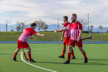 Male field hockey teammates celebrating with high fives on synthetic turf pitch holding sticks. Athletes, teamwork, athleticism, outdoor, sportive, competitive, victoryの写真素材