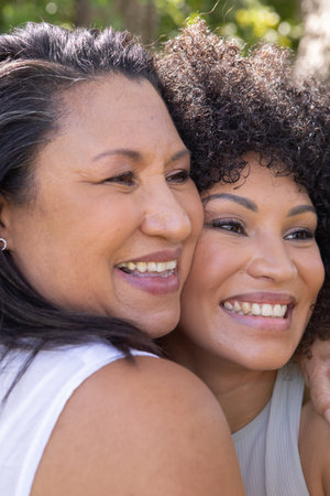 Senior mother and daughter pressing faces together outdoors in sunlit garden background. Emotional,...