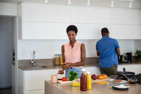 Diverse couple chopping tomato and greens while brewing coffee at kitchen island. Modern, culinary, lifestyle, minimalist, domestic, collaborative, vibrantの写真素材