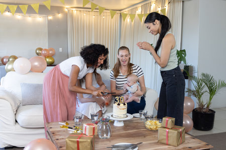 Diverse female friends cutting birthday cake with 30 candle in living room with balloons, gifts. Celebration, friendship, joy, warm, cozy, decor, partyの写真素材