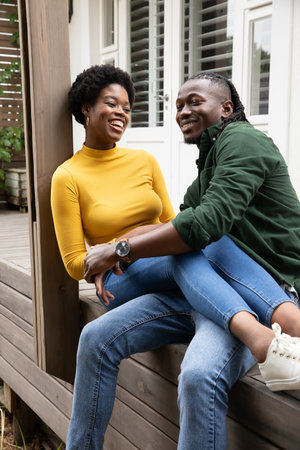 African American couple sitting close and smiling on porch bench with shuttered windows. Romantic, leisure, lifestyle, cozy, authentic, candid, outdoorの写真素材