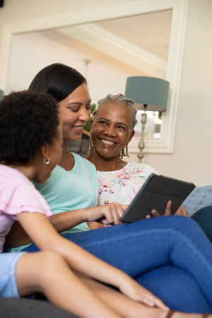 Diverse family sitting on sofa in living room interacting while using tablet computer together....