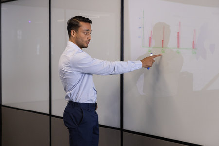 Asian man in business attire presenting bar chart using blue marker in conference room, copy space....