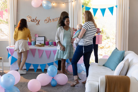 Diverse female friends celebrating at home living room shower party with pastel balloons and cake. Celebration, friendship, joy, decor, cozy, femininity, warmthの写真素材
