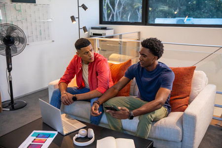 Diverse male colleagues discussing design concepts over laptop and phone mockups in office lounge....