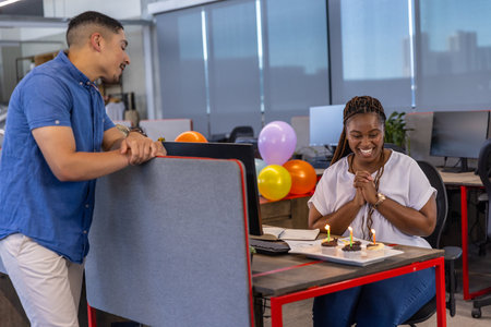 Diverse coworkers celebrating birthday in open-plan office with cupcakes and balloons, copy space. Collaboration, festivity, cheerful, modern, workplace, decor, friendshipの写真素材