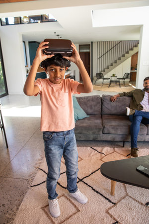 Indian father and son playing with virtual reality headset in modern living room on patterned rug....