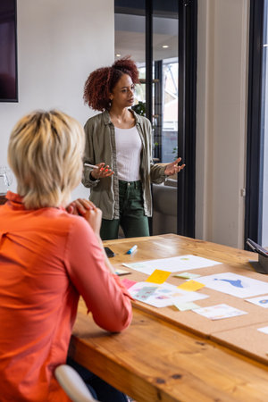 Diverse female coworkers discussing design mockups around conference table in office meeting room....