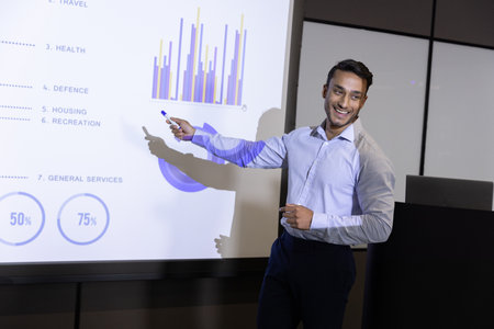 Indian man gesturing with marker at projection screen showing chart and diagram, copy space....