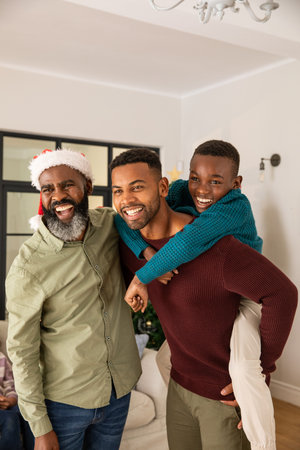 African American family standing and smiling in living room beside Christmas tree wearing Santa hat....