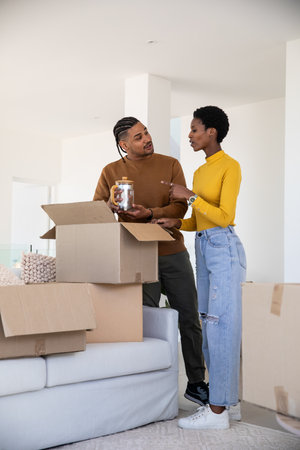 African American couple unpacking boxes at home while examining glass jar filled with corks....