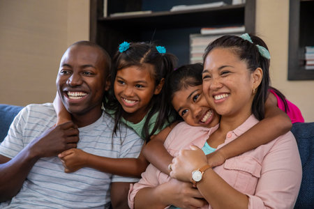 Diverse family sitting on blue couch in living room hugging and smiling with bookshelf background....