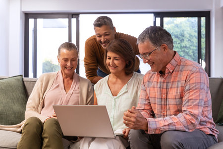 Family of four sitting on sofa in bright living room, viewing silver laptop together. Group, home,...