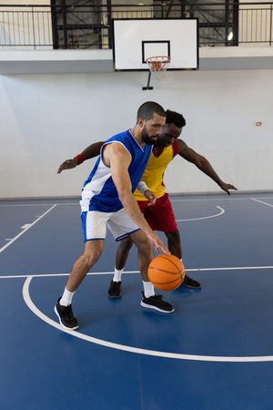 Two male athletes dribbling and guarding on gym basketball court with hoop and orange basketball. Sports, competition, teamwork, fitness, athleticism, training, energetic