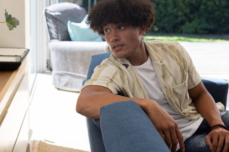 African American man relaxing on blue armchair at home while gazing through sliding glass door....