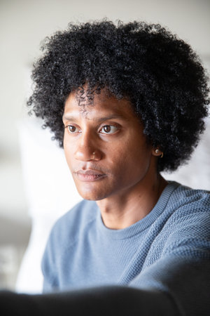African American man sitting on sofa in living room wearing light blue sweater by white cushion....