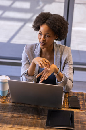 African American woman presenting idea in office with laptop mobile devices coffee cup wristwatch....