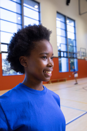 African American teenage girl smiling and looking right in gym by basketball court lines. Athlete, sport, activity, fitness, youthful, energy, teamworkの写真素材