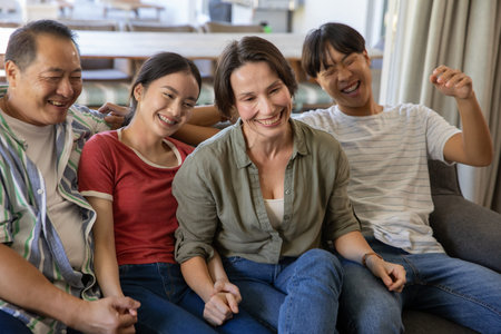 Diverse family sitting on sofa in living room in casual clothes holding hands, wristwatch showing....