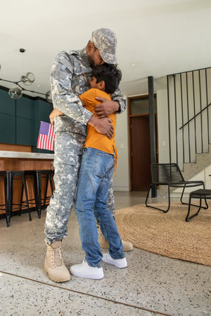 Soldier father and son hugging in home kitchen by wooden island. Military, family, affection,...