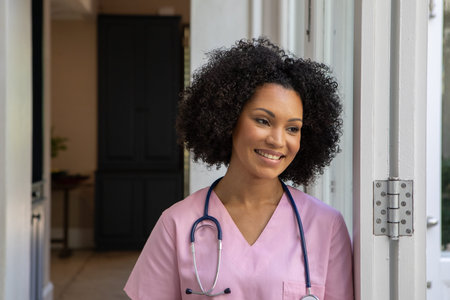 African American woman nurse standing leaning against white clinic doorway holding stethoscope....