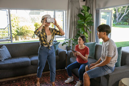Diverse family playing VR using headset and wireless controller on gray sofa over patterned rug. Technology, innovation, leisure, modern, connection, lifestyle, relaxationの写真素材