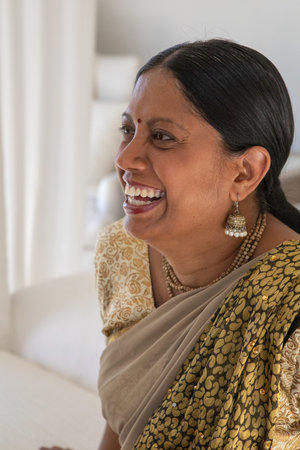 Mature Indian woman laughing while wearing cream sari, jhumkas and red bindi at home. Elegant,...