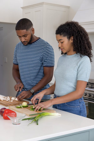Diverse couple chopping vegetables on kitchen island using wooden cutting boards and chef knives....