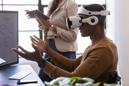 Diverse coworkers interacting using VR headset and tablet at office desk near monitor, copy space....