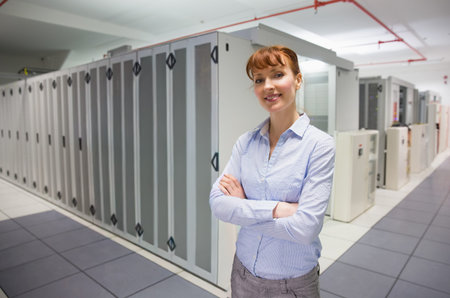 Female technician standing arms crossed in blue shirt gray pants at data center racks, copy space....