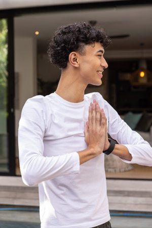 Man in white shirt and black smartwatch pressing palms together on wooden patio near glass door....