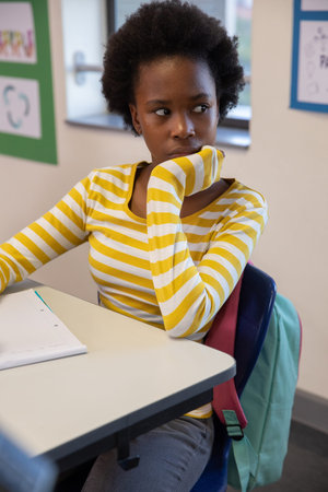 African American teenage student sitting and looking right at desk with open notebook, backpack....