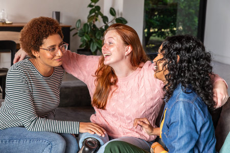 Diverse female friends sitting on sofa leaning near plant showing prosthetic leg in living room....