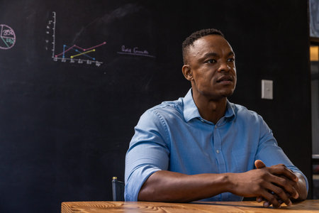 African American man wearing light blue shirt studying chalk diagrams at wooden table, copy space....