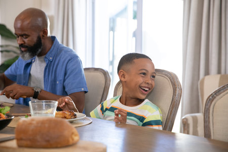 African American father and son sharing lunch in home dining room with roasted chicken, copy space....