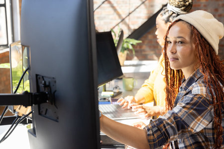 Diverse coworkers adjusting monitor and typing on laptop at desk in open plan office, copy space....