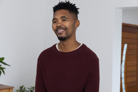 African American adult man standing, looking right in entry wearing maroon sweater and hoop earring....