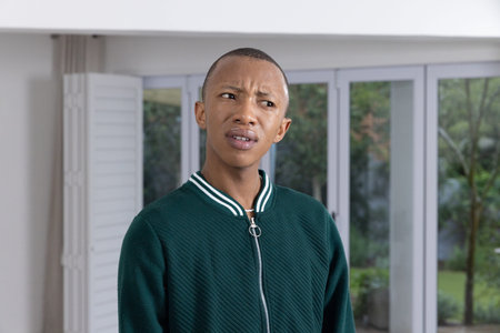 African American man standing by glass doors and shutters wearing quilted jacket, looking puzzled....