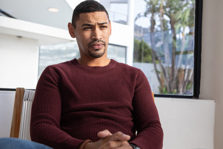African American man sitting in woven chair at office gazing through window at palm trees....