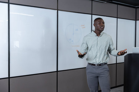 African American man presenting at whiteboard beside podium with laptop in meeting room, copy space....