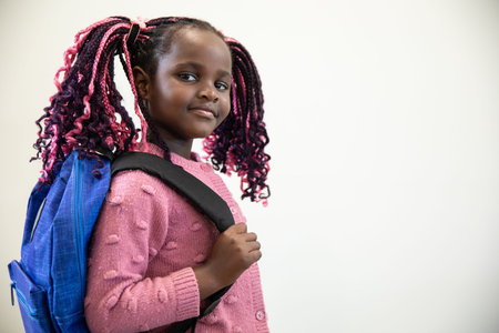 African American girl posing in studio wearing pink cardigan carrying blue backpack, copy space....