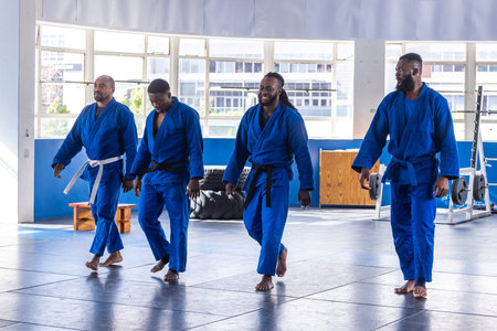 African American male martial artists walking barefoot across mat in training studio with blue gis....