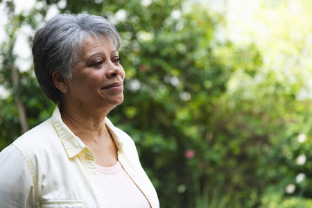 Senior African American woman standing in garden wearing stud earrings gazing right, copy space....
