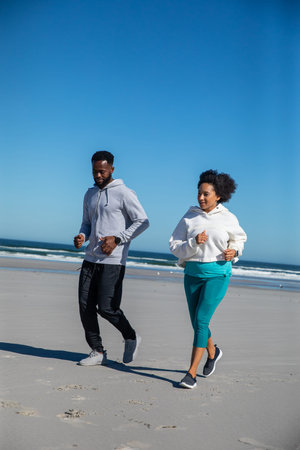 Diverse friends running along sandy shoreline wearing running shoes, smartwatch and fitness tracker....
