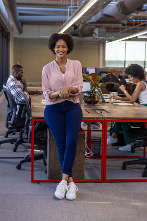 African American colleagues smiling and working at open-plan office desk with laptops and tablet....
