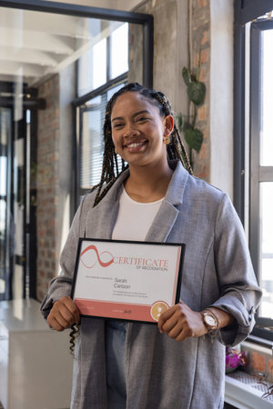Smiling woman wearing blazer in office while holding certificate of recognition. Achievement,...
