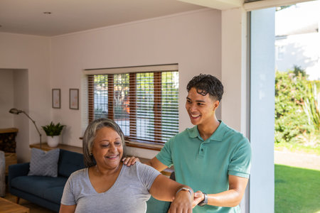 Stretching arms senior mother and son in living room by sliding glass door near sofa. Family,...